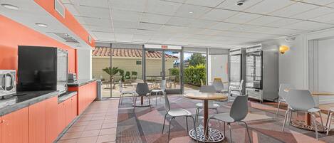 A modern indoor dining area with orange and white walls, a tiled floor, and a mix of round and square tables with chairs.