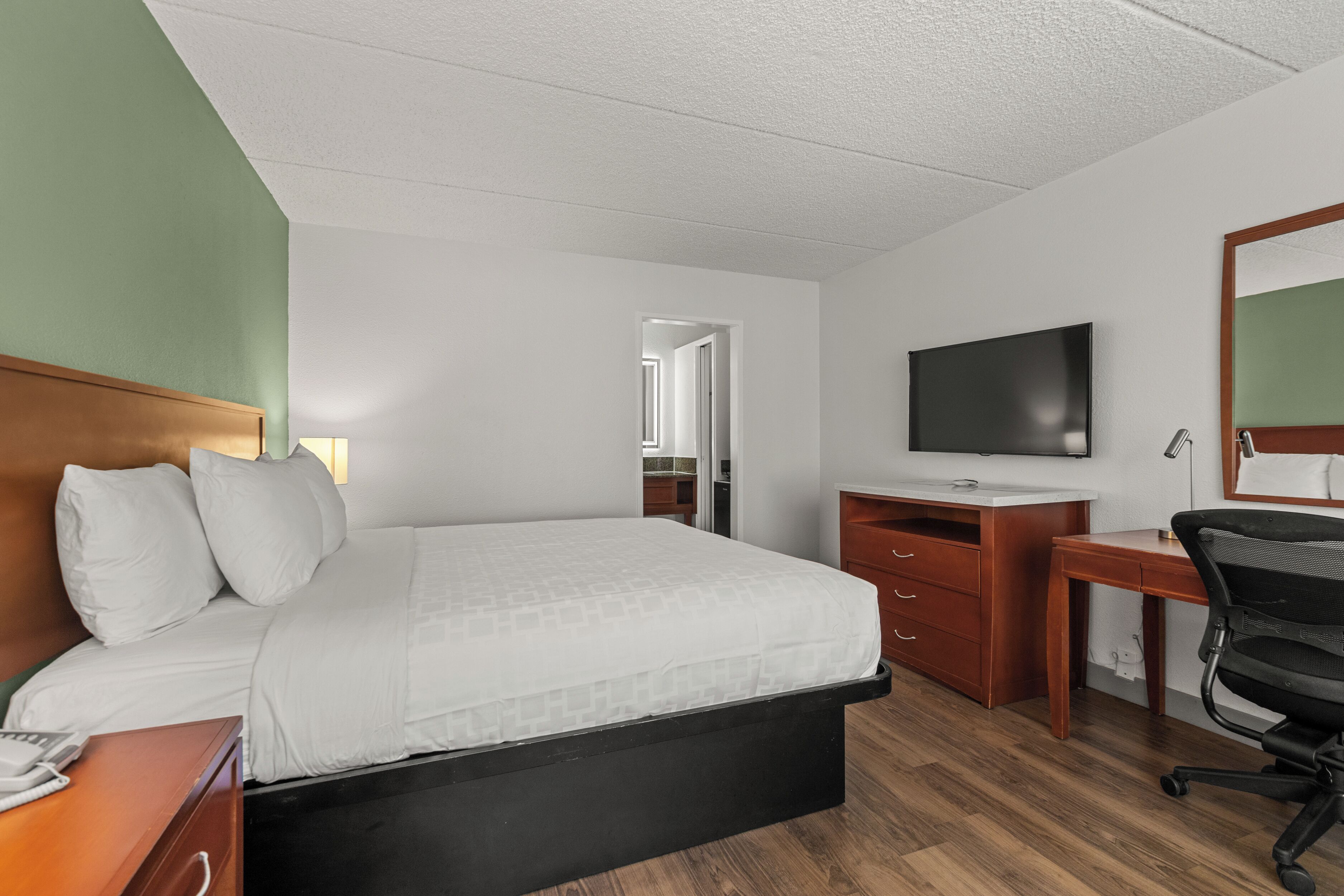 A hotel room with a bed, a desk, a chair, a television, and a mirror.