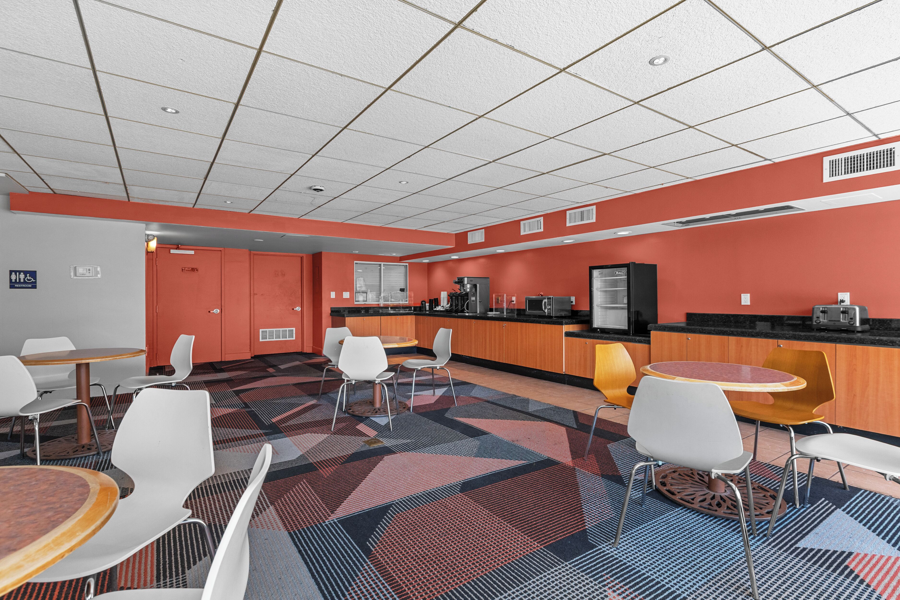 Een moderne hotellobby met een centrale zithoek, een kitchenette en een receptiebalie.