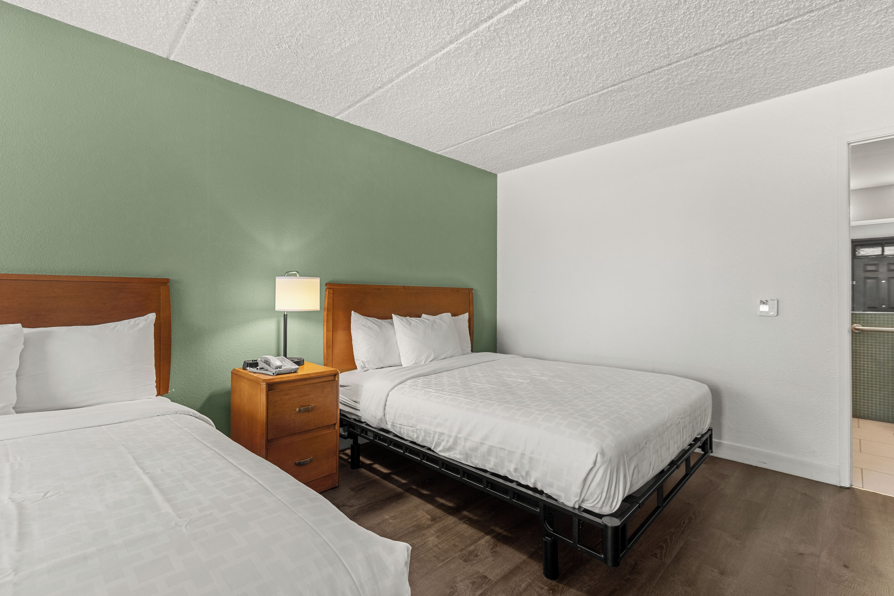 A hotel room with two beds, a nightstand with a lamp, and a view of a balcony.