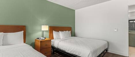A hotel room with two beds, a nightstand with a lamp, and a view of a balcony.
