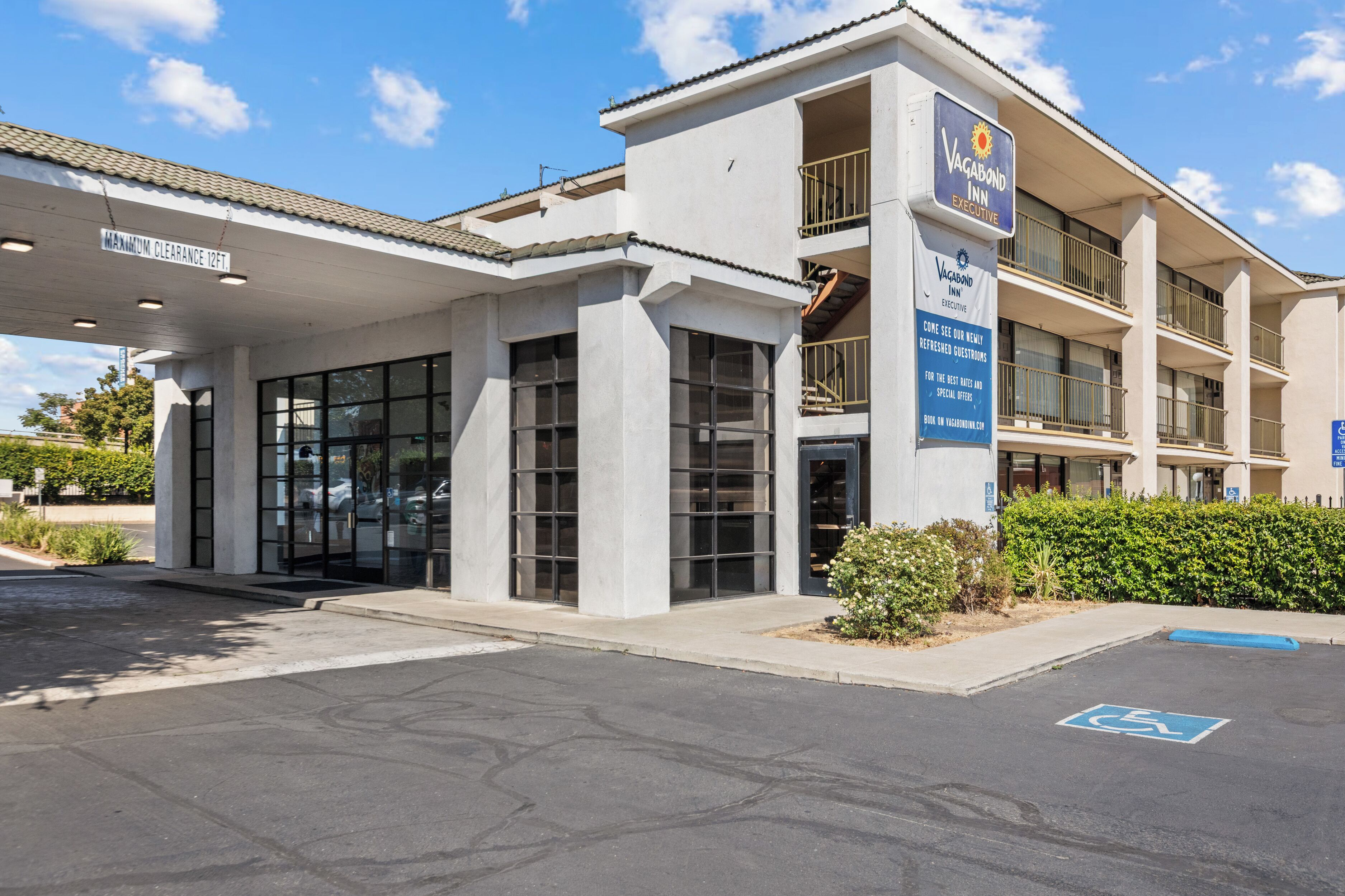 A modern building with a sign for Vagabond Inn Executive. It has a covered entrance, multiple balconies, and a parking lot with a handicapped parking space.