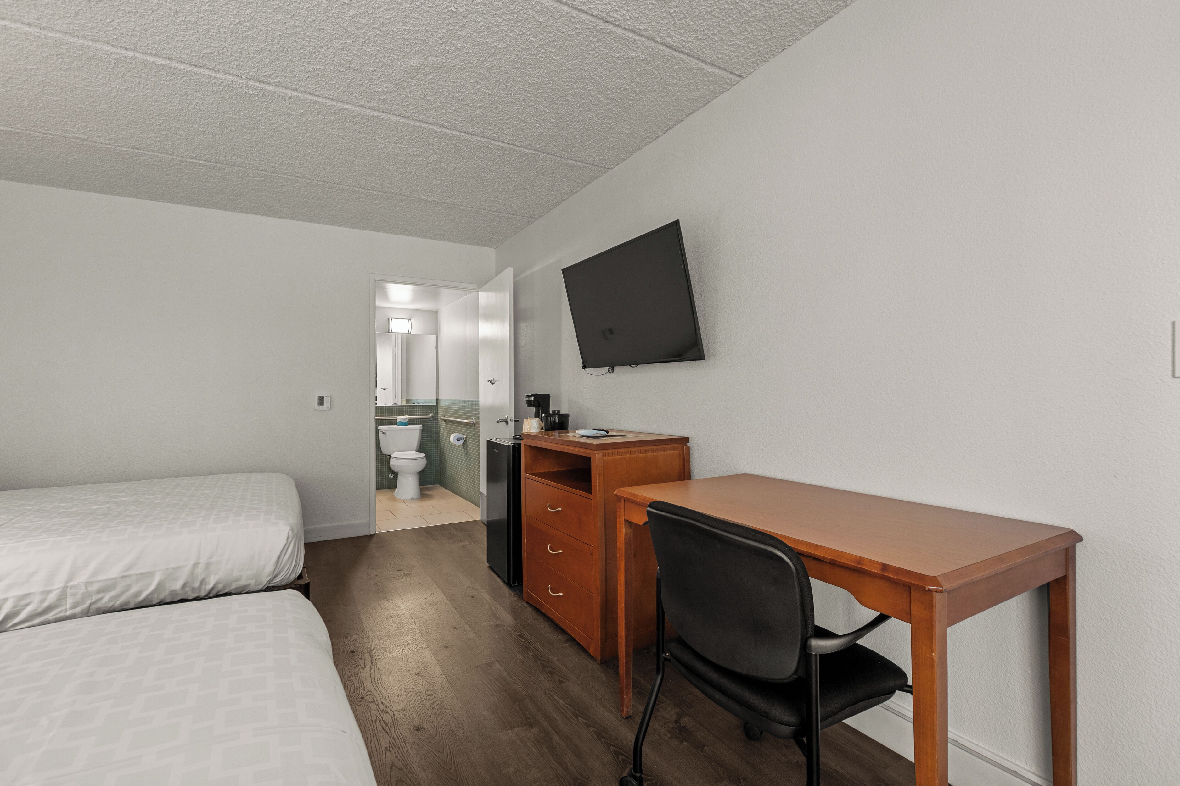 A hotel room with a bed, a desk, a chair, a television, and a small kitchenette.