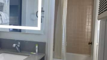 A bathroom with a sink, mirror, and shower area.