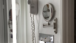 Une salle de bain équipée d’un miroir, d’un sèche-cheveux, d’un miroir rond et d’un porte-serviettes.