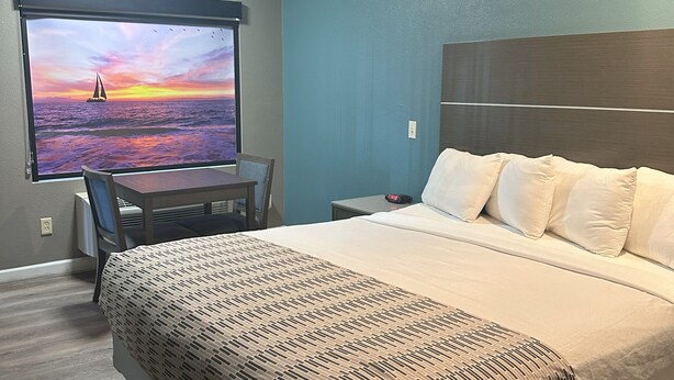 Une chambre d’hôtel comprenant un lit, un bureau avec une chaise, une table de chevet et un téléviseur fixé au mur qui diffuse une scène de coucher de soleil.