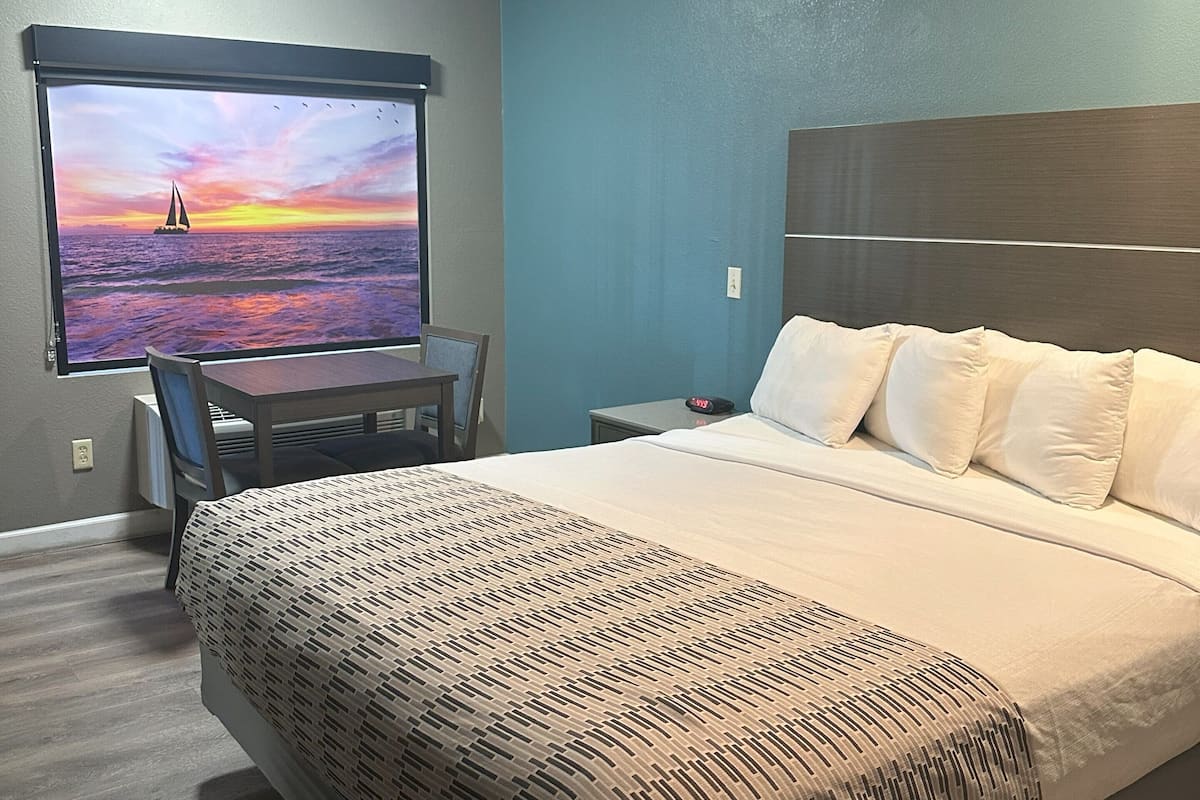 Une chambre d’hôtel comprenant un lit, un bureau avec une chaise, une table de chevet et un téléviseur fixé au mur qui diffuse une scène de coucher de soleil.