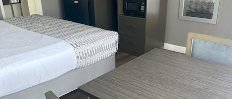 A hotel room with a bed, a desk with a flat-screen TV, a microwave, and a small refrigerator.