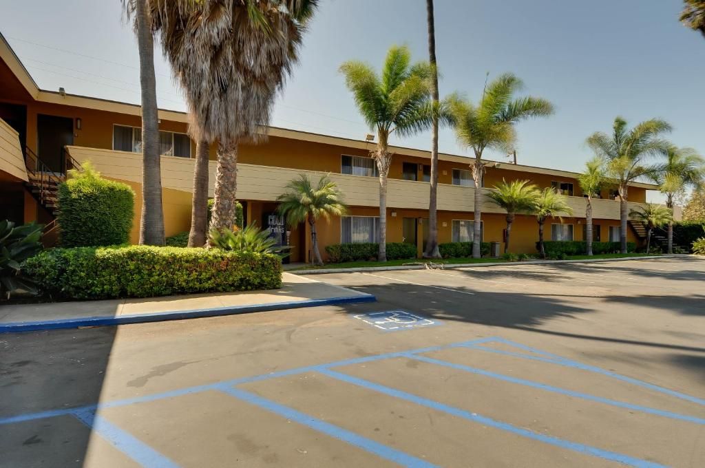 Un hotel con una hilera de habitaciones, un estacionamiento y palmeras.
