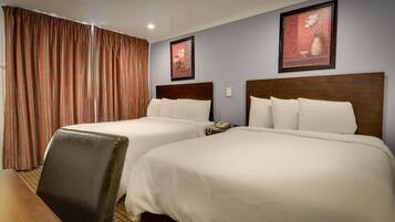 A hotel room with two beds, a wooden desk, and a chair.