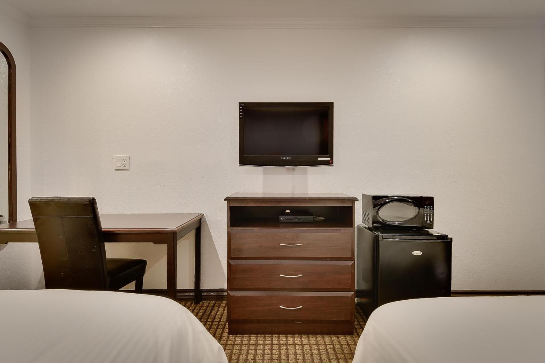 A hotel room with two beds, a desk with a chair, a wooden dresser, a television, and a microwave.