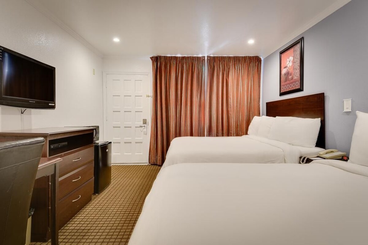 A hotel room with a bed, a desk with a television, a door, and a curtain.