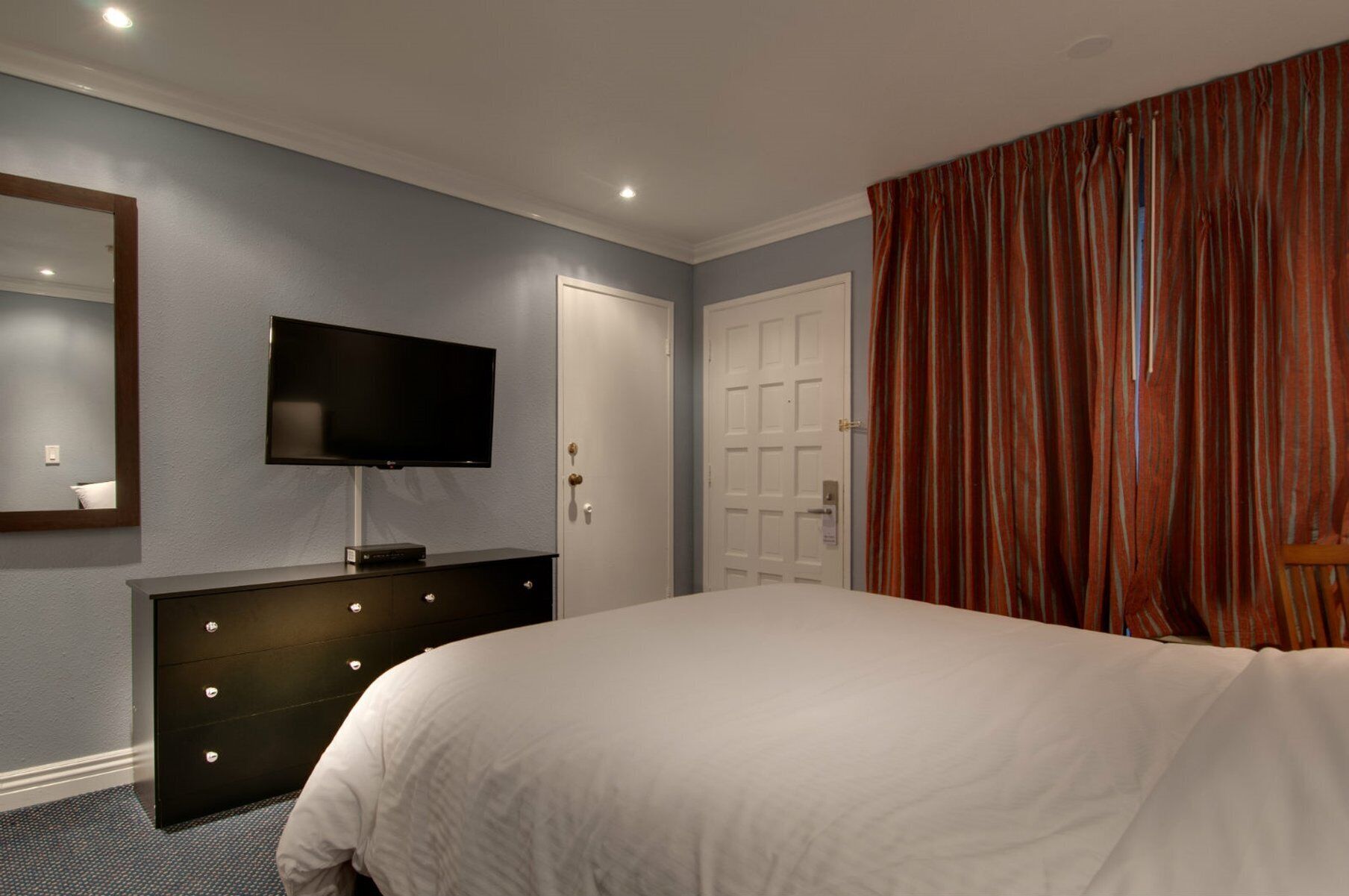 A bedroom with a bed, a dresser, a television, and a door.