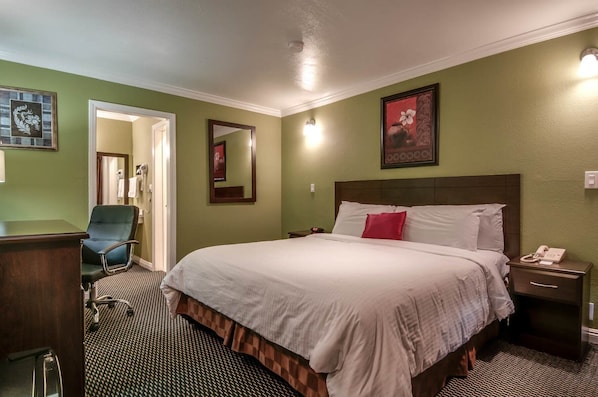 A hotel room with a large bed, a desk, a chair, a mirror, and a telephone.