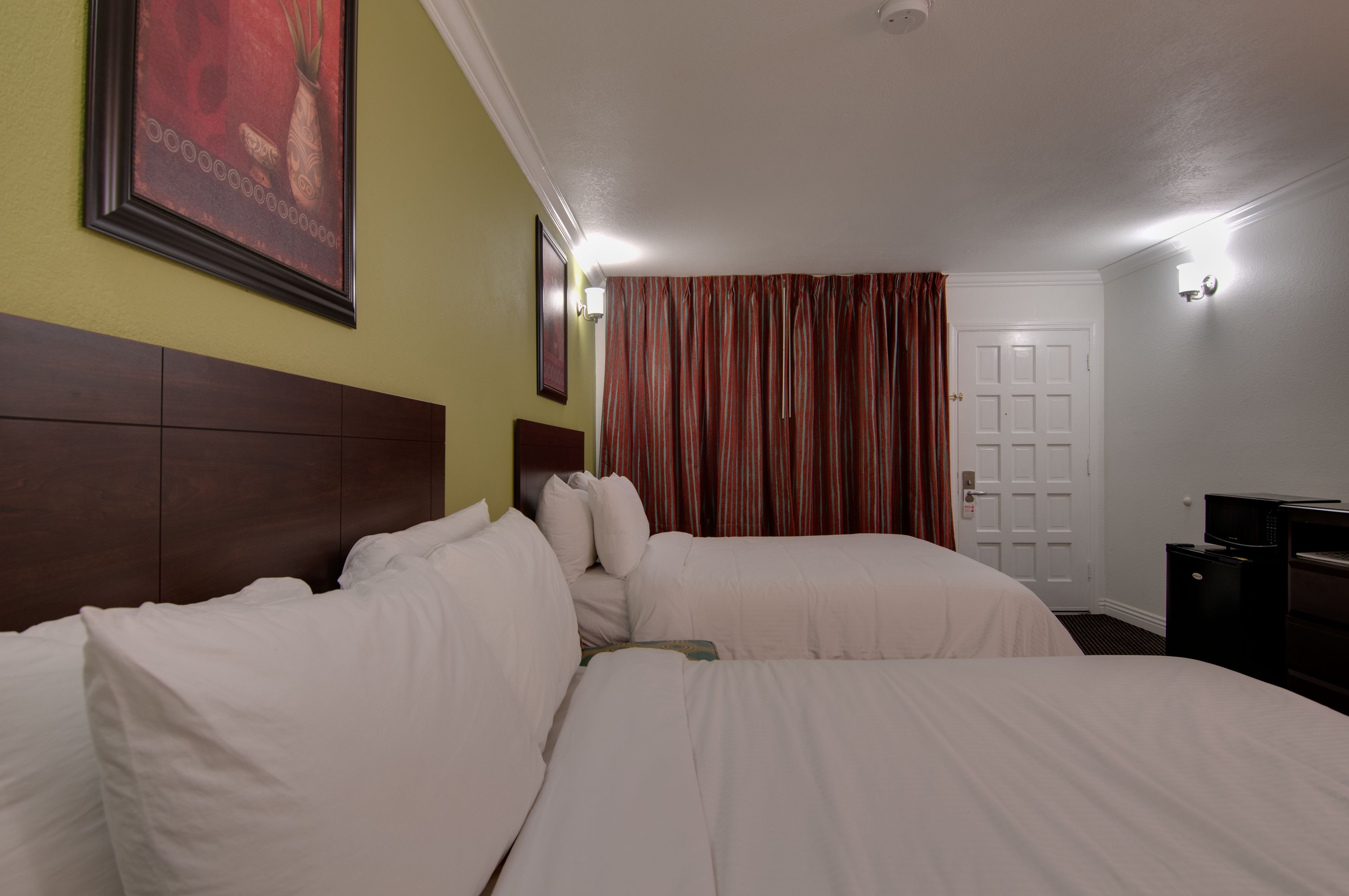 Une chambre d’hôtel avec deux lits, une tête de lit en bois, une porte et un petit bureau avec un four à micro-ondes.
