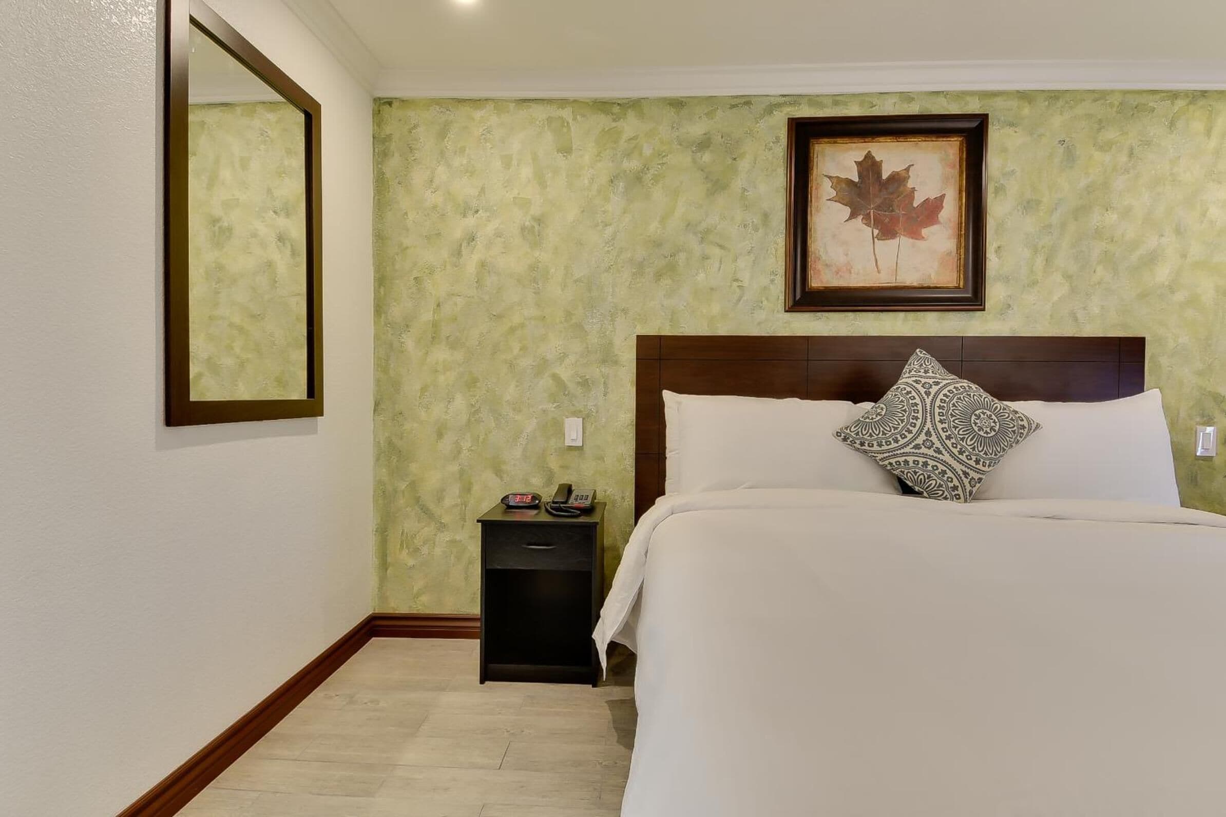 Quarto de hotel com uma cama, uma mesa de cabeceira, um quadro na parede e um espelho.