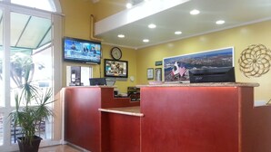 A reception area with a red counter, a clock, a television displaying news, and a framed picture of a cityscape.