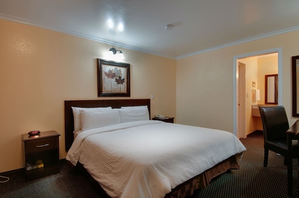 A hotel room with a large bed, a nightstand, a desk, and a chair.