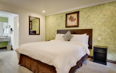 A hotel room with a large bed, a bedside table, a mirror, a framed picture on the wall, and a bathroom visible through an open door.