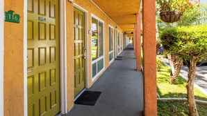 A hotel corridor with green doors, numbered room 116, and a covered walkway with a small tree and hanging plants. - Vagabond Inn Costa Mesa (Costa Mesa)