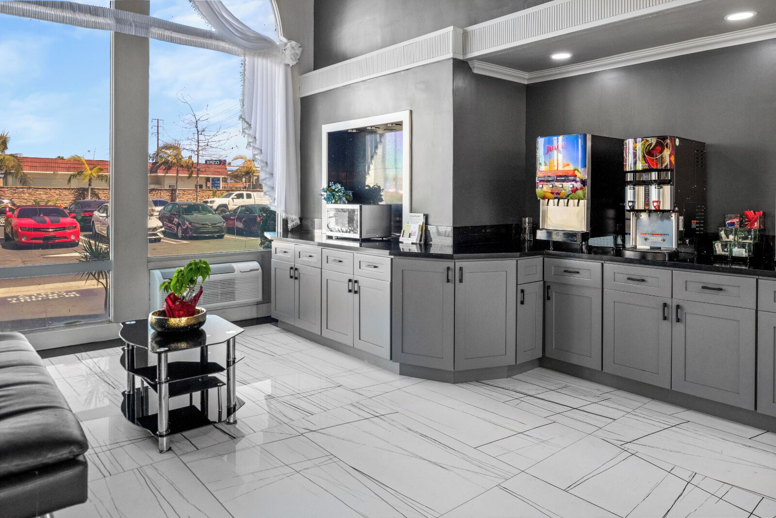 A modern kitchen with grey cabinets, a black countertop, and a window overlooking a parking area. - Vagabond Inn Costa Mesa (Costa Mesa)