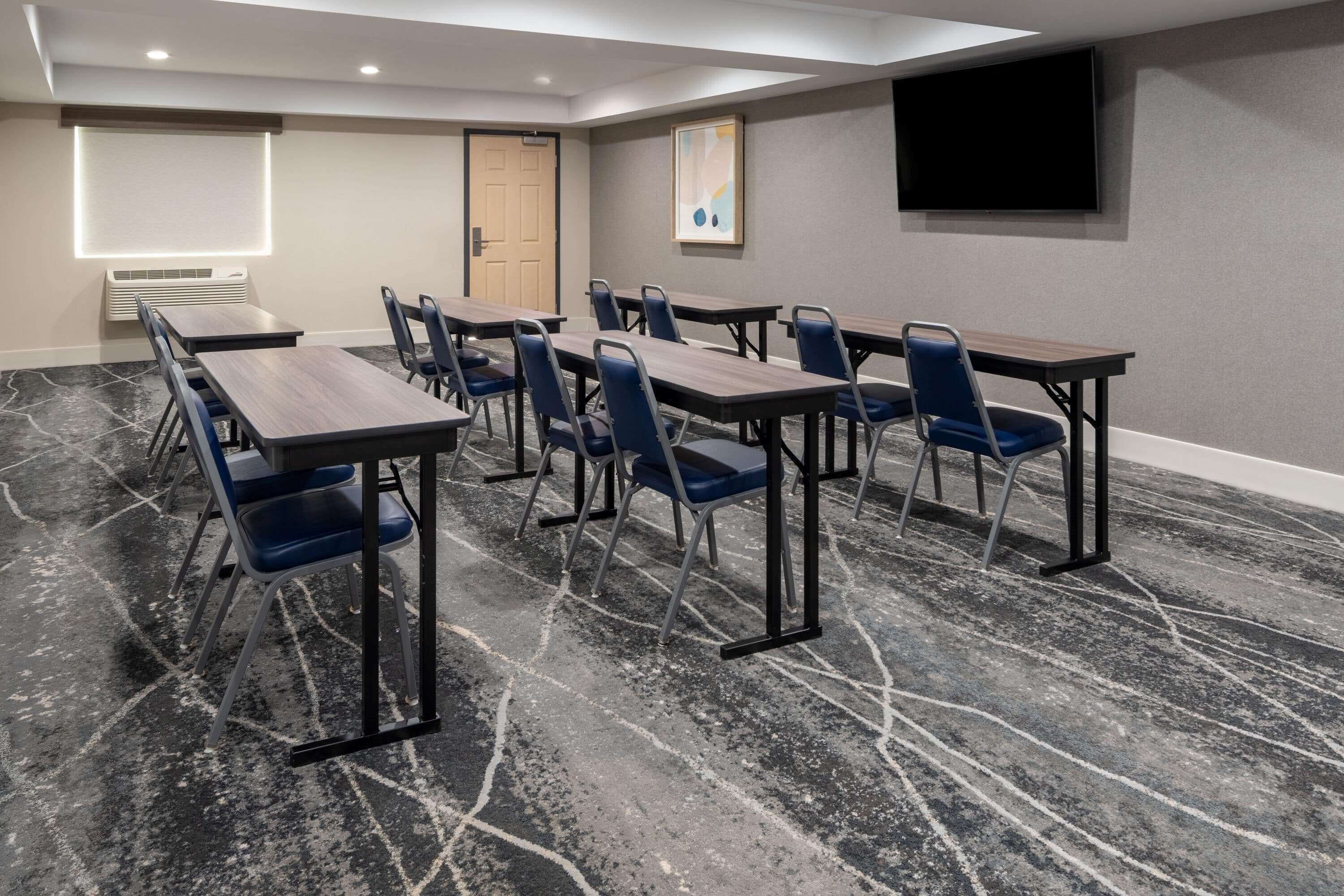 A conference room with a marble floor, multiple tables and chairs, a projector screen, and a flat-screen TV on the wall.