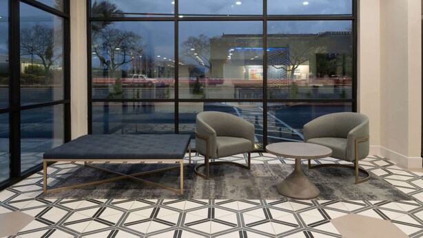 Un intérieur moderne avec de grandes fenêtres, un sol à motifs géométriques, ainsi que deux fauteuils et une petite table.
