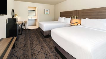 A hotel room with two beds, a desk, a chair, a television, and a bathroom.