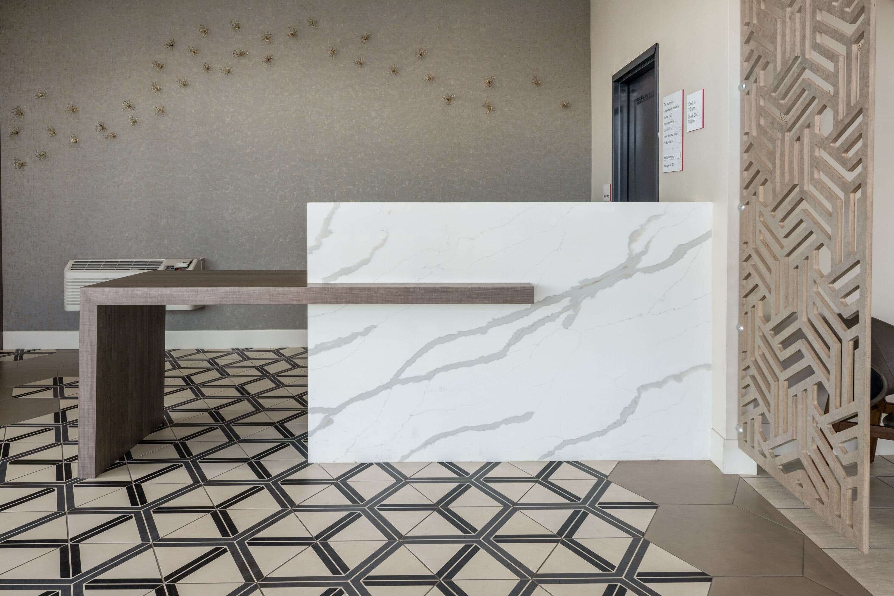 Una zona de recepción con un mostrador de mármol, baldosas de suelo con estampado geométrico y una pared con un panel decorativo.