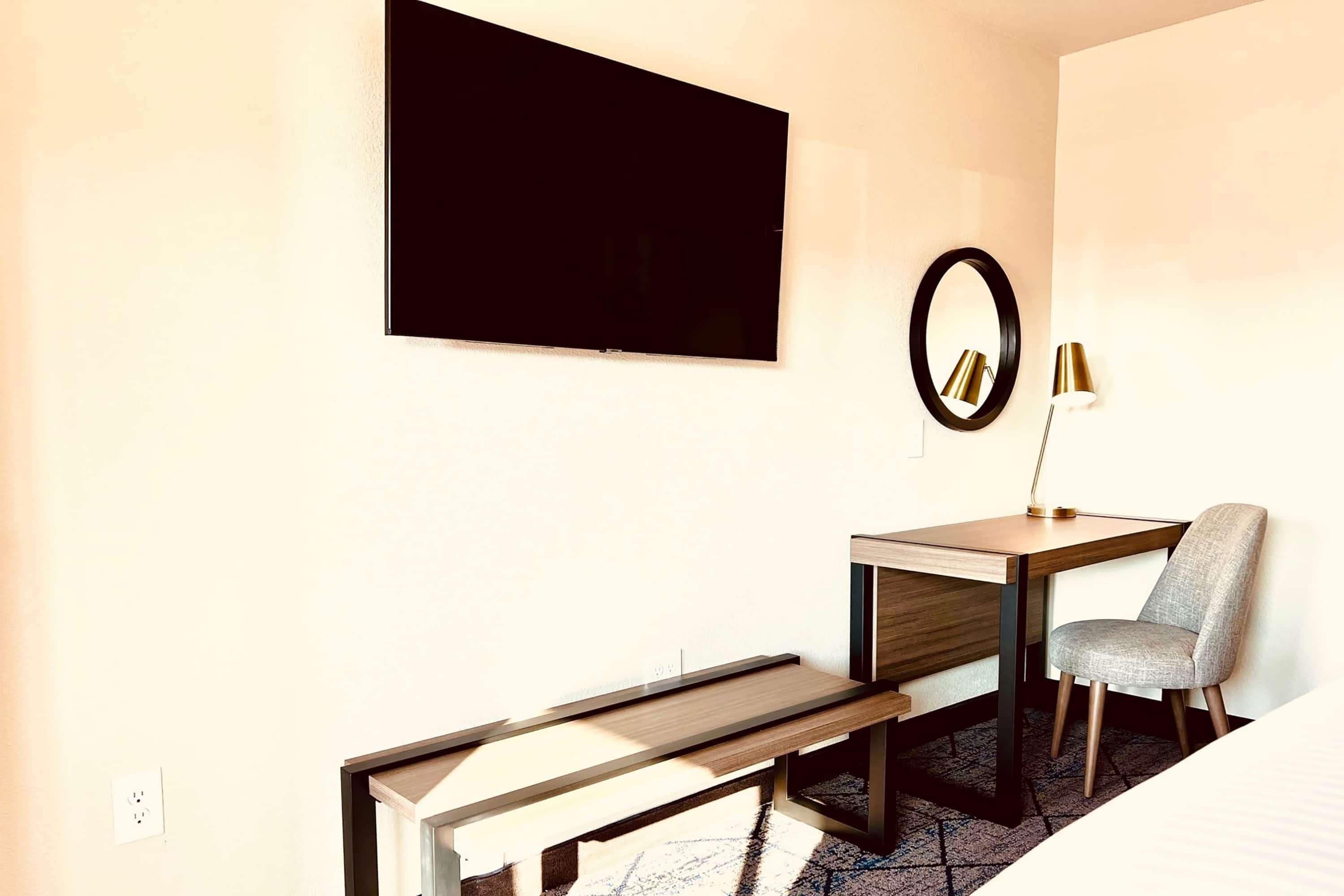 A modern hotel room with a desk, chair, and a large mirror.