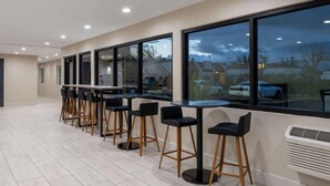 Un espace bar moderne avec des tables et des tabourets hauts, de grandes fenêtres et une vue sur l’extérieur.