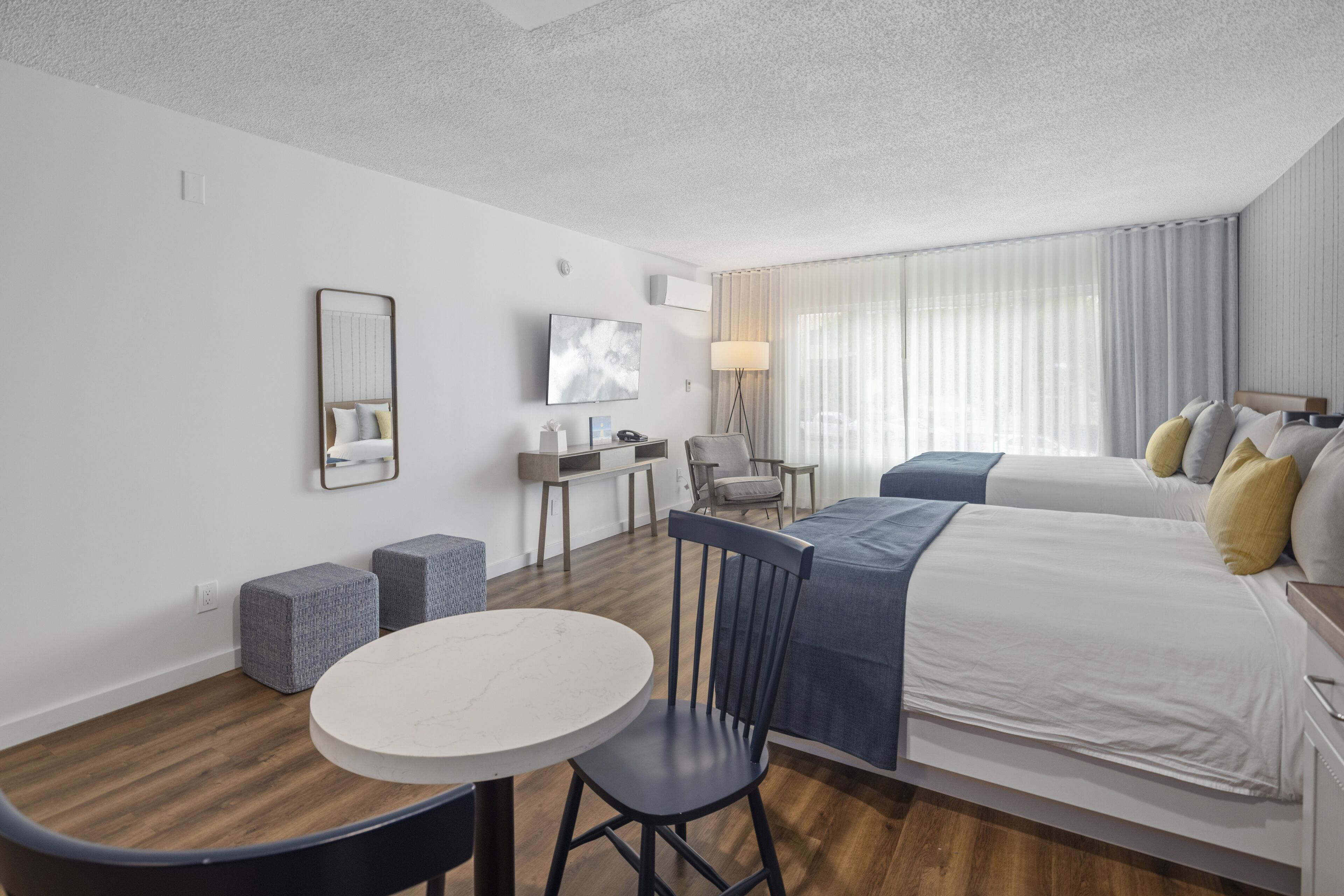 Une chambre d’hôtel moderne avec un plancher en bois, une table ronde, deux lits, un bureau et une chaise.