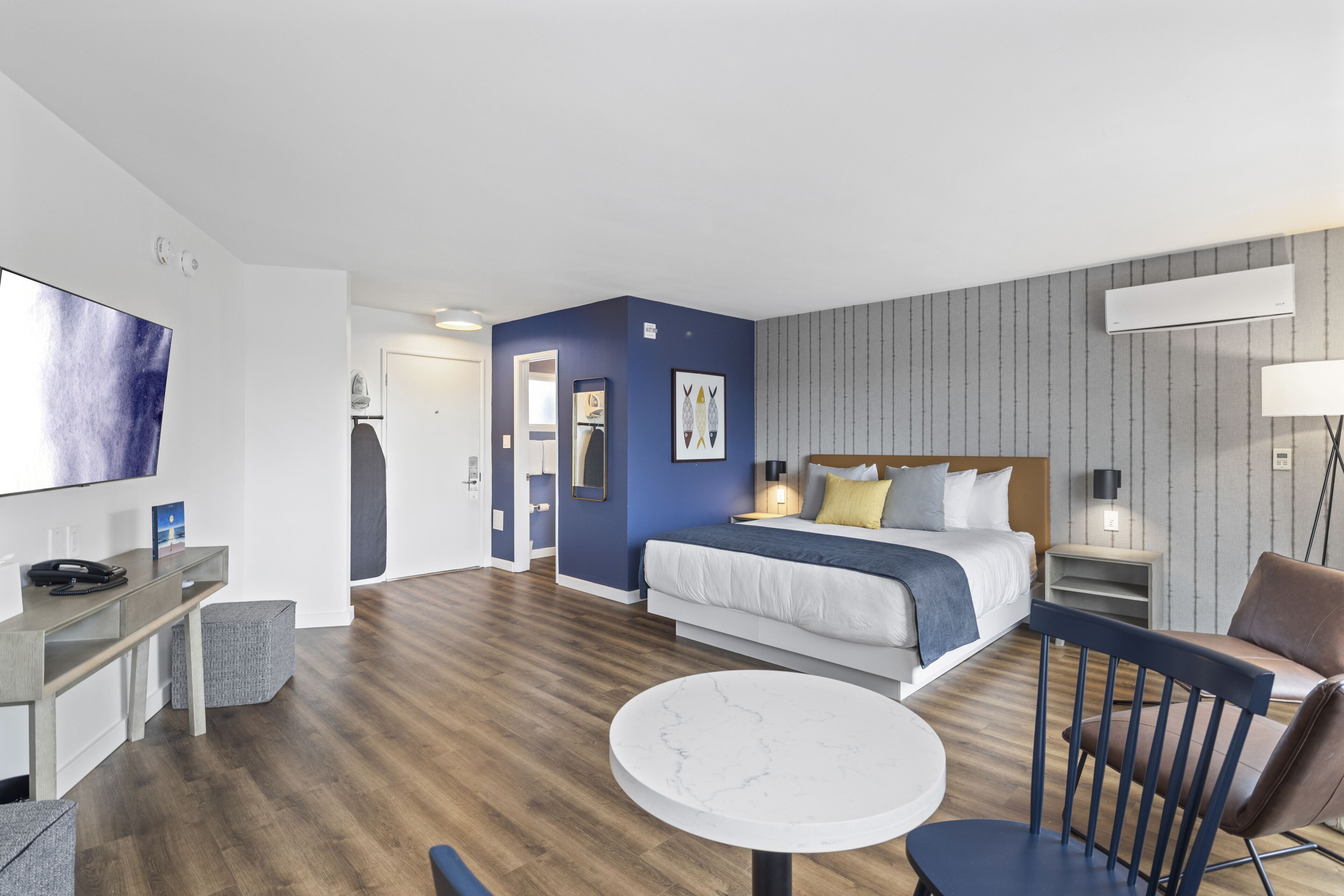 A modern hotel room with a large bed, a desk, a chair, and a round table.