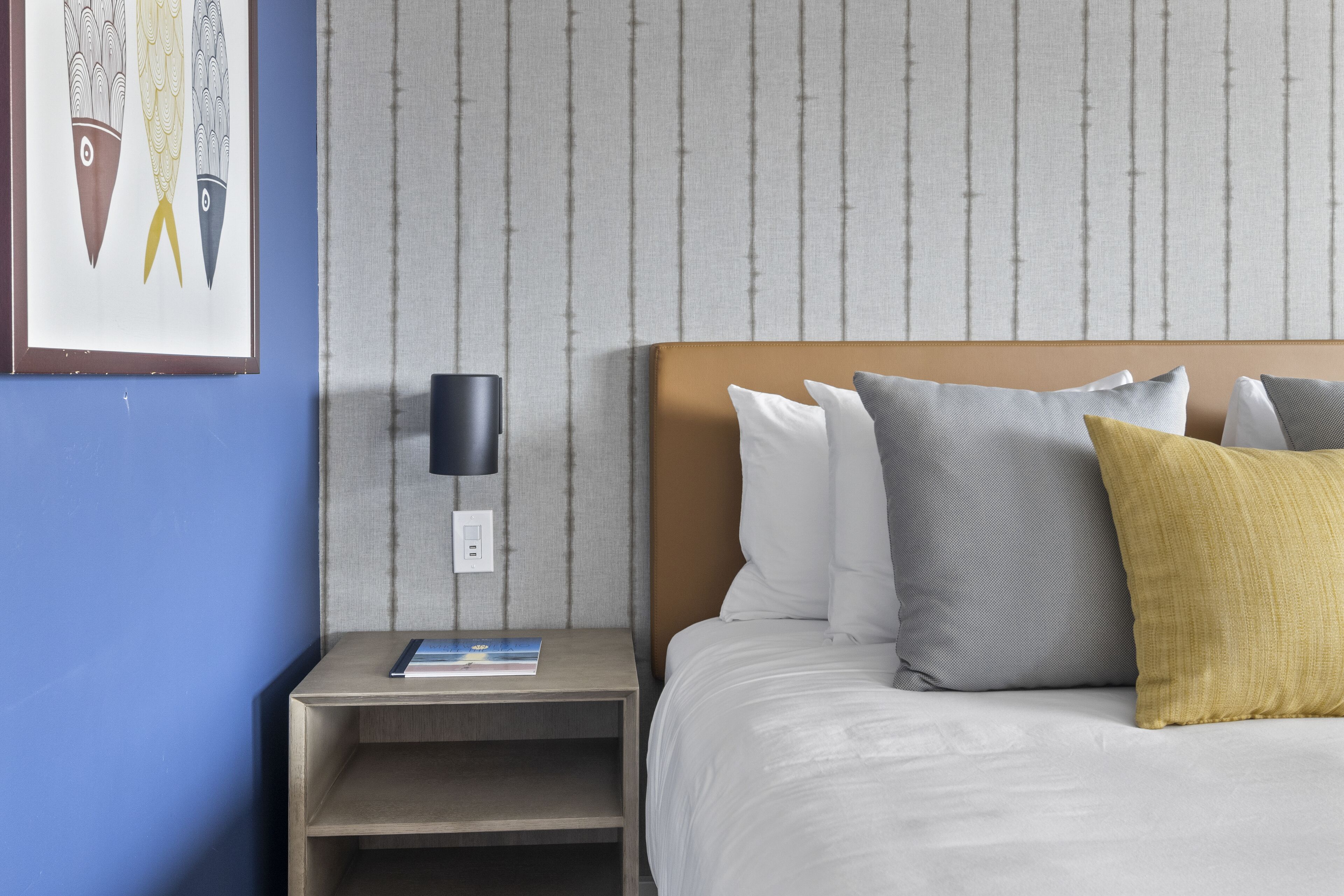 Een hotelkamer met een bed, kussens, een nachtkastje, een lamp en een ingelijst schilderij aan de muur.