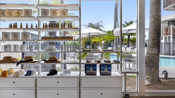 A well-lit retail area with shelves displaying various products, a poolside view, and a palm tree. - Sea Harbor Hotel (San Diego)