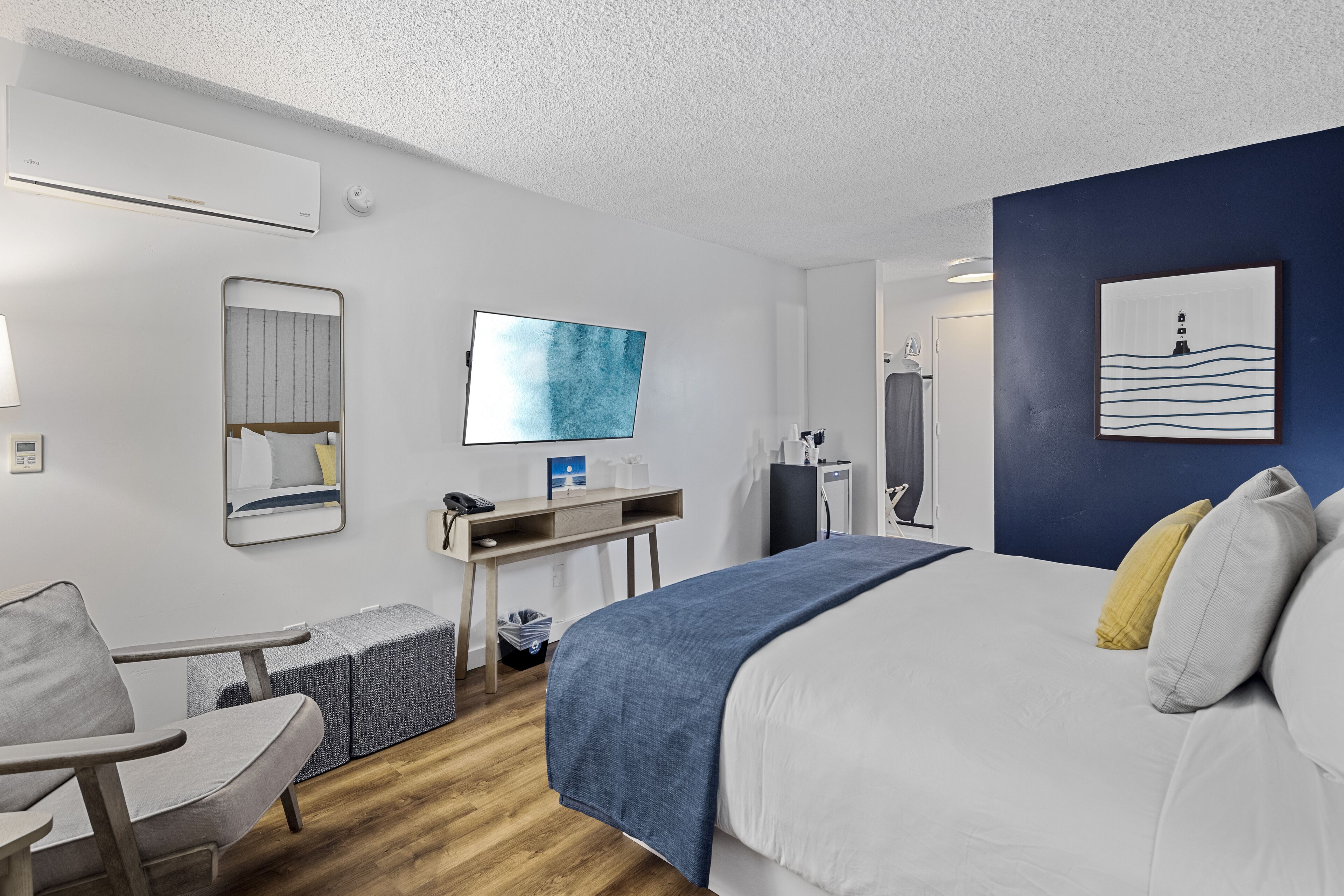 Quarto de hotel moderno com uma cama grande, uma escrivaninha com cadeira, televisão de tela plana e banheiro visível por uma porta aberta.