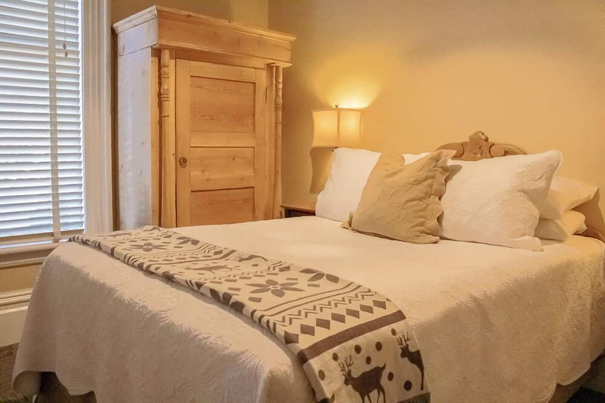 A neatly made bed with a patterned blanket, a wooden wardrobe, and a bedside lamp.