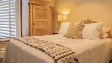 A neatly made bed with a patterned blanket, a wooden wardrobe, and a bedside lamp.