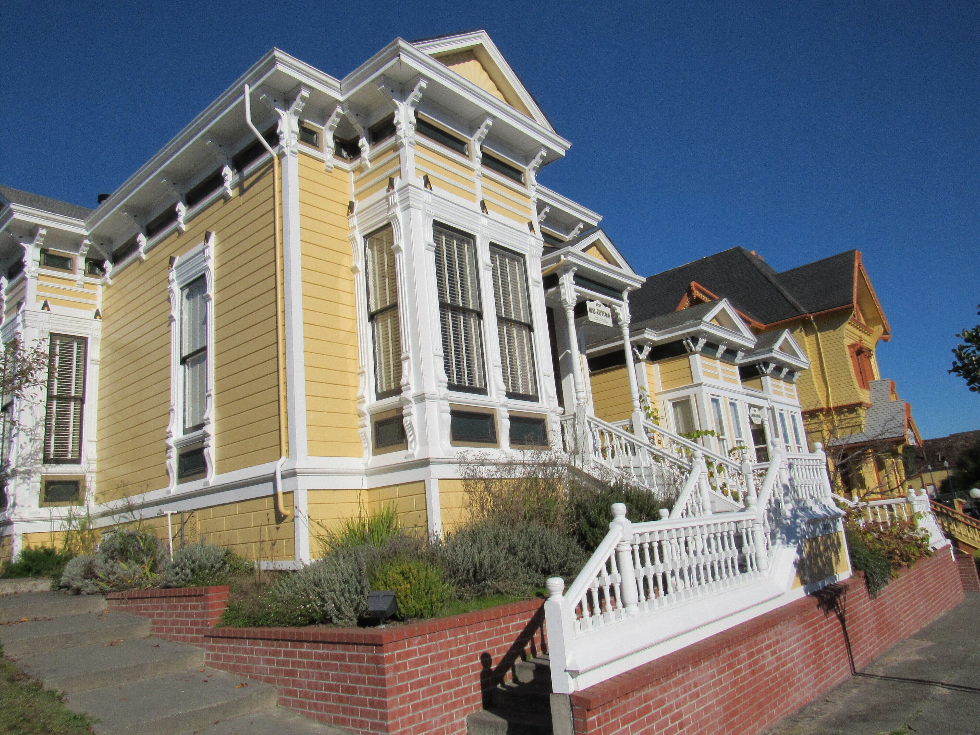 A yellow Victorian-style house with a white porch and brick steps.