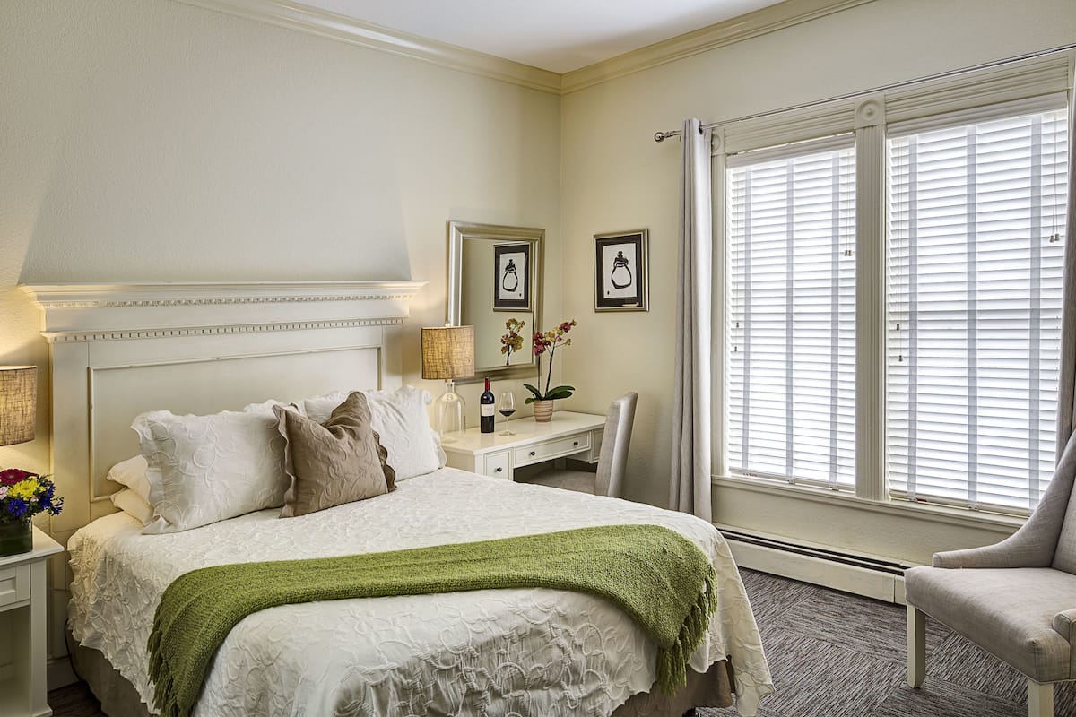 A neatly arranged bedroom with a large bed, bedside tables, a desk, and a chair.