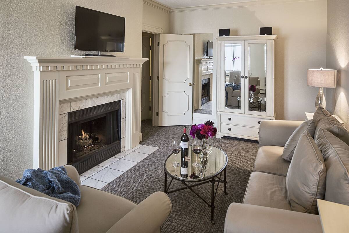 A living room with a fireplace, a television, a sofa, a coffee table with wine glasses, and a cabinet.