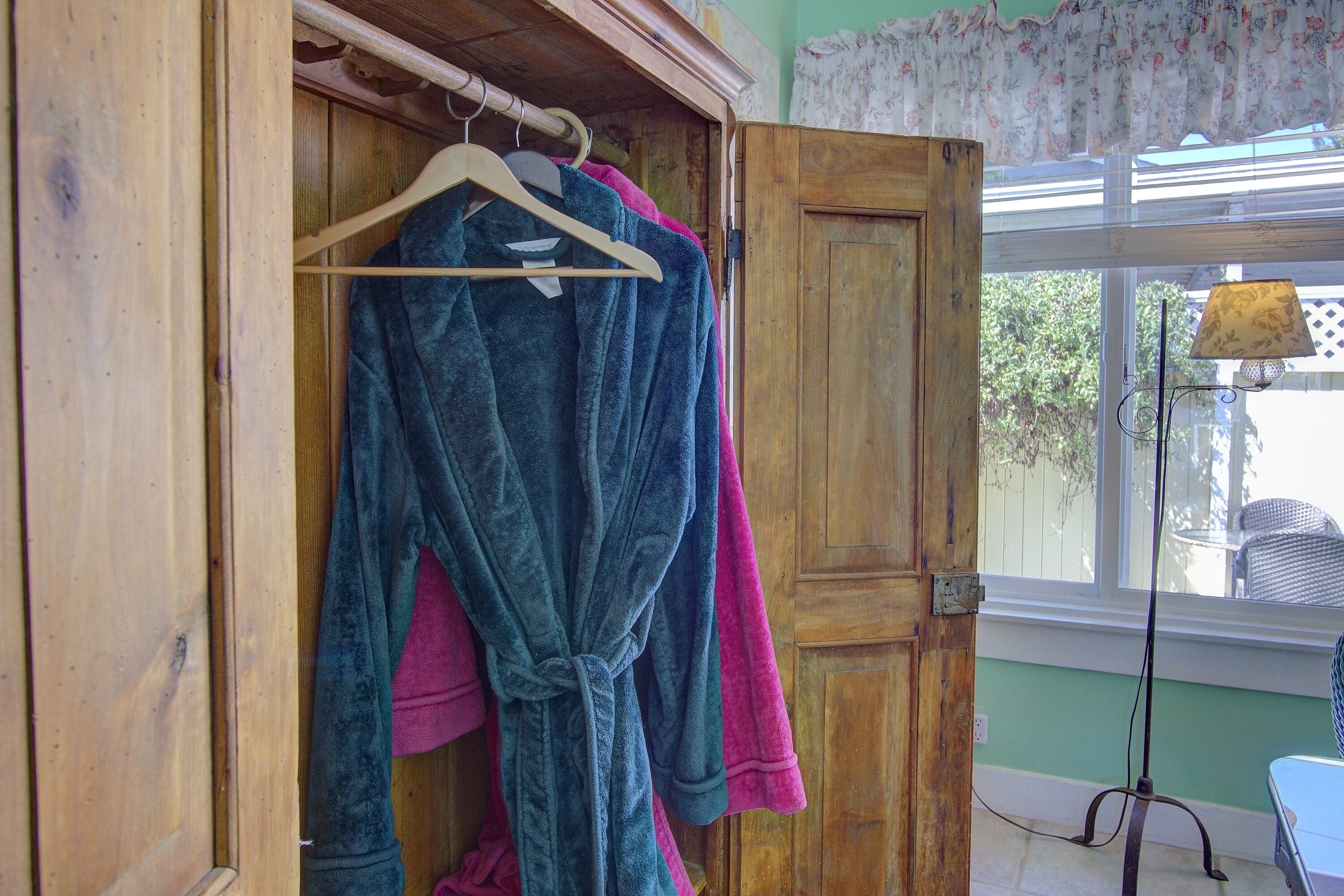 Une armoire en bois avec une tringle où sont suspendues une robe bleue et une robe rose.