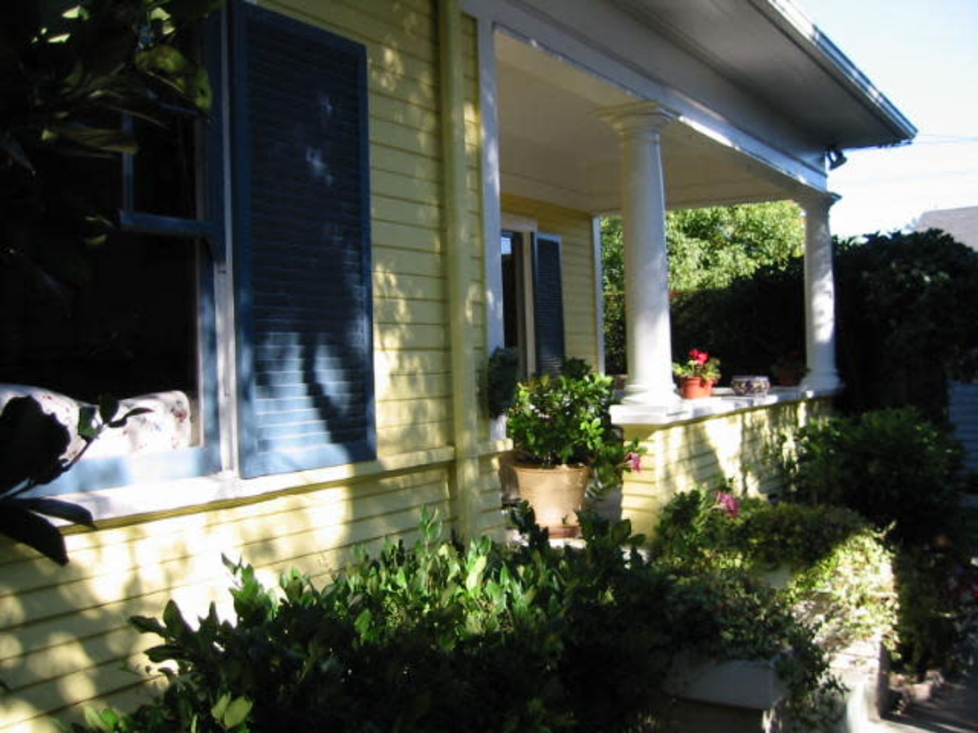 A yellow house with a covered porch, columns, and potted plants.