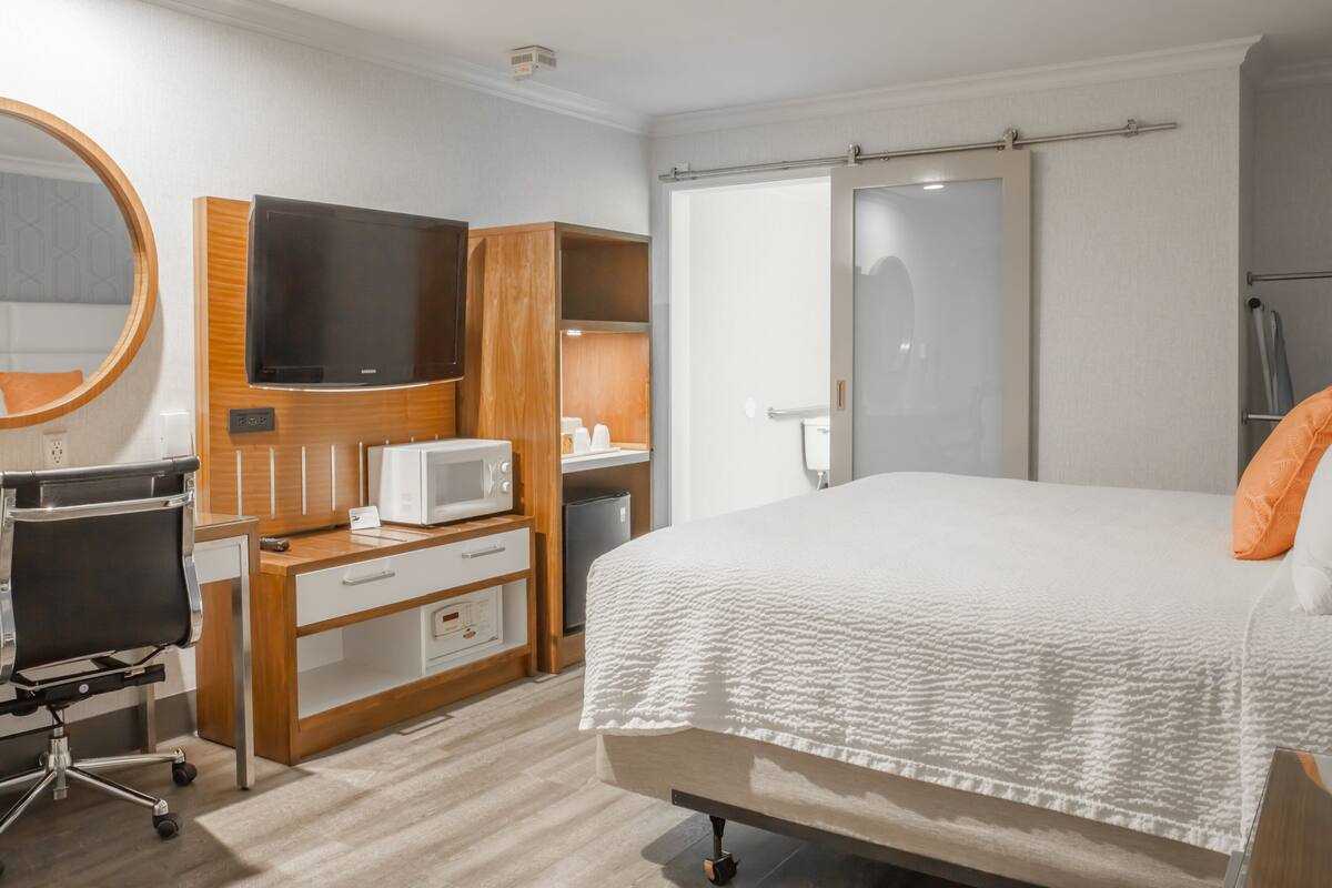 A hotel room with a bed, a desk with a computer, a microwave, and a TV.