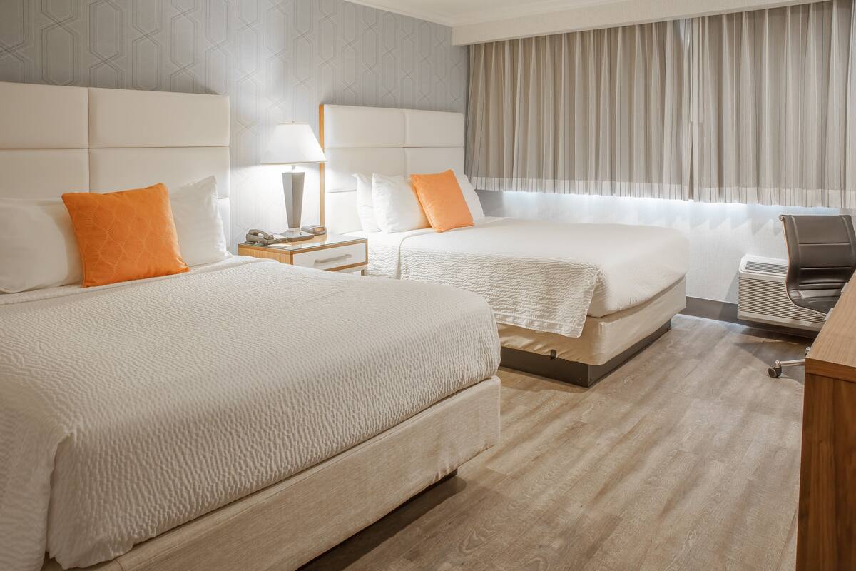 A hotel room with two beds, a desk, a chair, and a window with curtains.