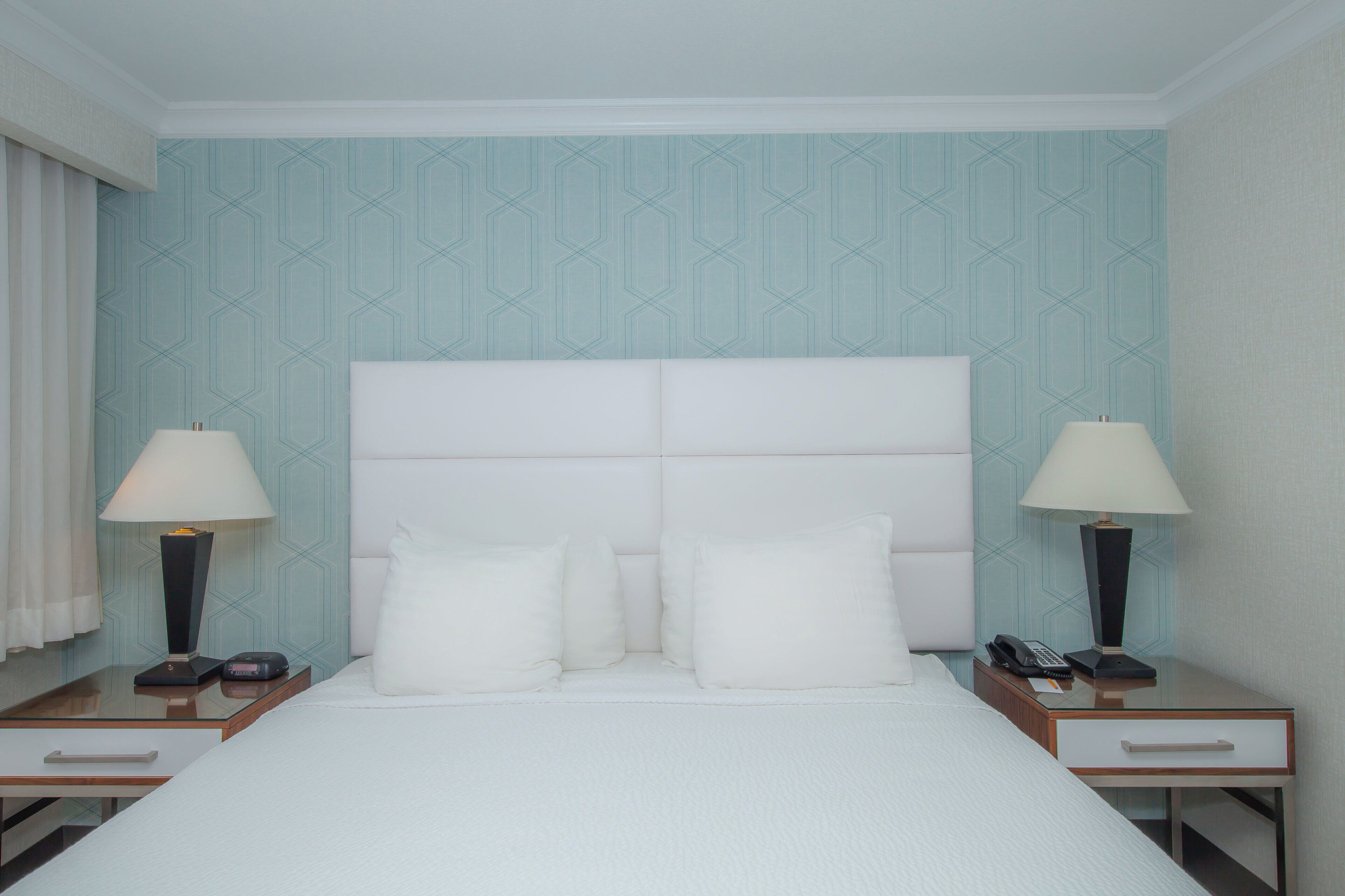 Ein Hotelzimmer mit einem großen Bett, zwei Nachttischen, zwei Lampen und einer Wand mit Muster.