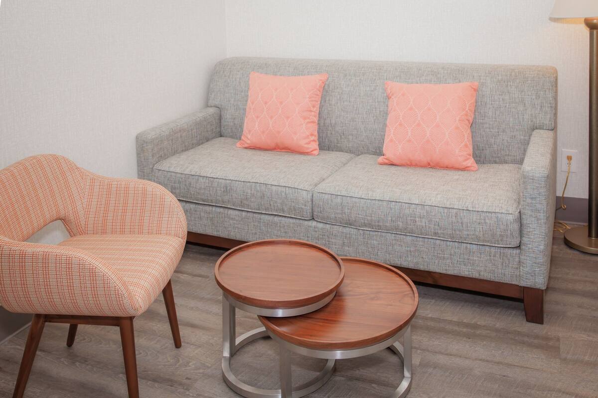 A grey sofa with two matching cushions, a wooden chair, and two round wooden side tables.
