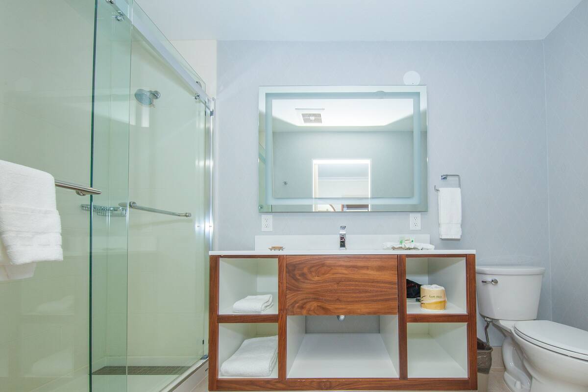 A bathroom with a glass shower enclosure, a wooden vanity with a mirror, and a toilet.