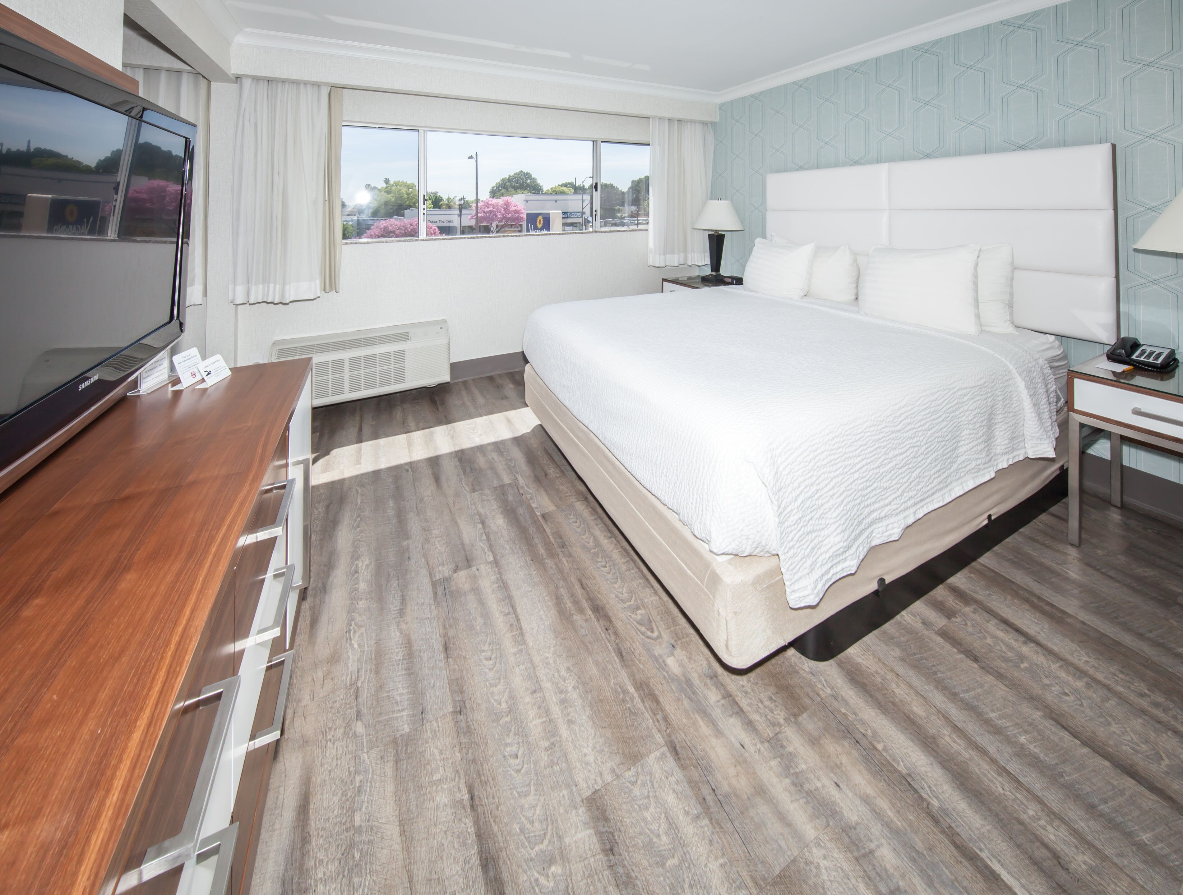 Habitación de hotel con una cama grande, televisión, escritorio y ventana con cortinas.