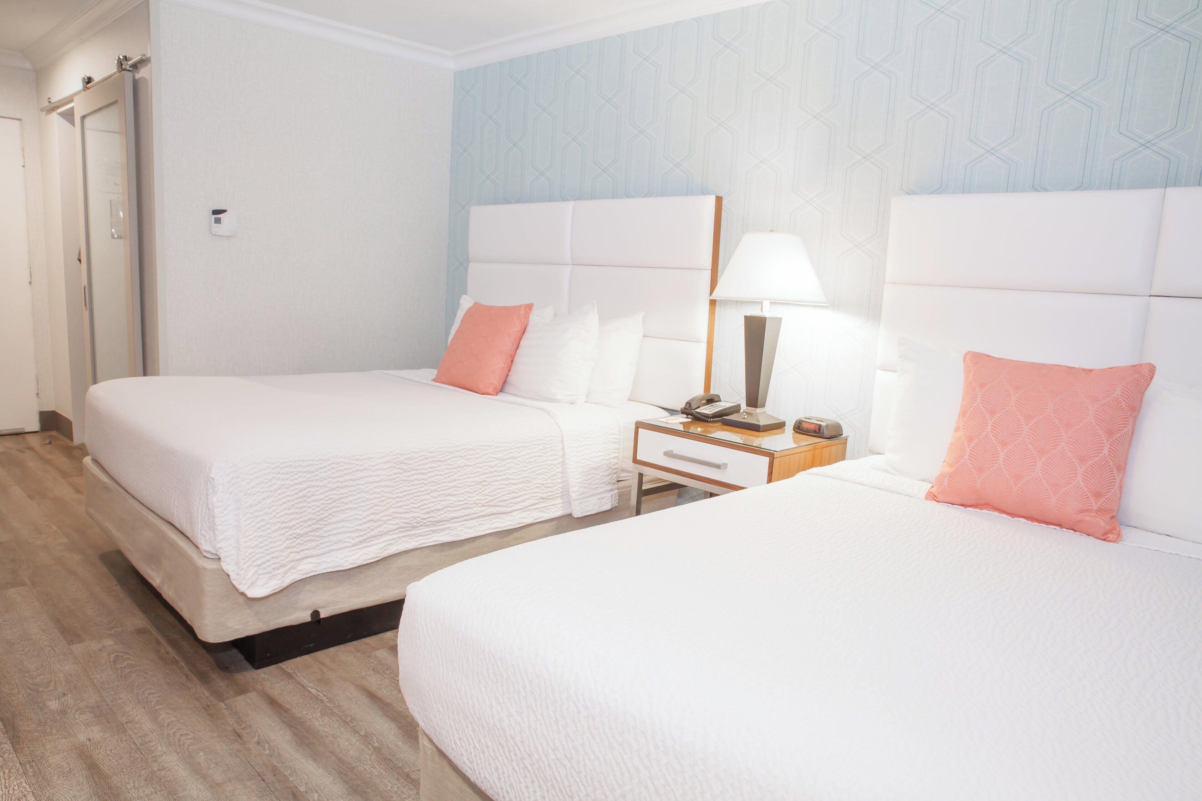 Una habitación de hotel con dos camas, una mesita de noche con lámpara y un espejo.